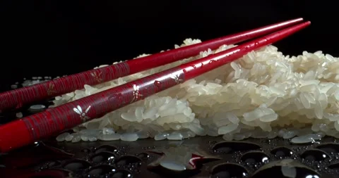 Red chopsticks with pattern lie on wet rice with drops of water around on Black Stock Footage 142768062