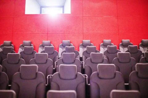 A red cinema interior with empty soft seats and a projector on the screen Stock Photos