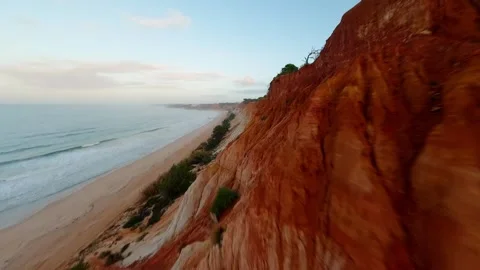 Red cliffside cliffs drop to ocean waves at golden hour Video stock 346090361