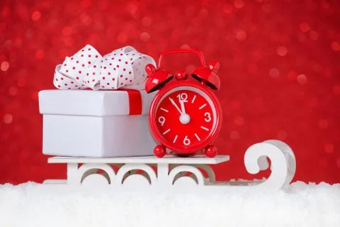 Red clock with a gift box over sleigh in snow on red background Stock Photos