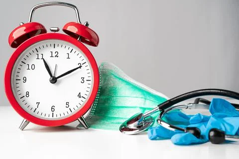 Red clock, green protective face mask, stethoscope and gloves. Stock Photos