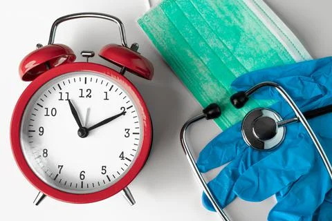 Red clock, green protective face mask, stethoscope and gloves. Stock Photos