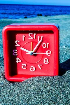 A red clock with the numbers 1 to 12 on it is sitting on a beach Foto stock