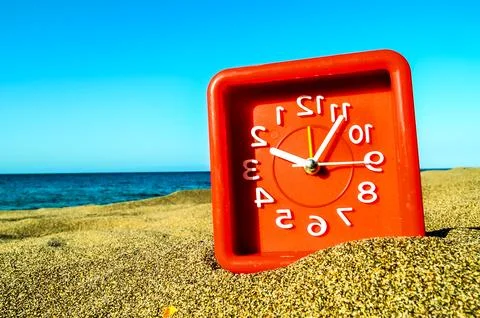 A red clock is sitting on the sand next to the ocean Foto stock