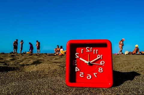 A red clock is sitting on the sand next to a beach Foto stock