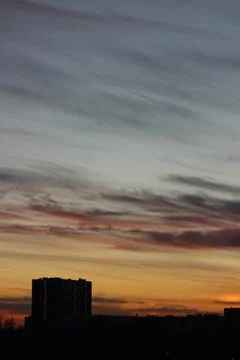 Red clouds between blue and yellow sky over a dark city Stock Photos