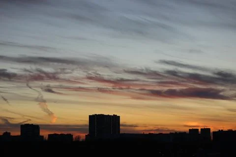 Red clouds between blue and yellow sky over a dark city Foto stock