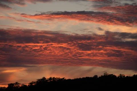 Red clouds lit up by the sun at sunset. Stock Photos