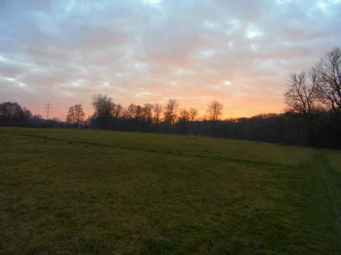 Red cloudy dusk over meadow behind distant forests in snowless winter. Stock Photos