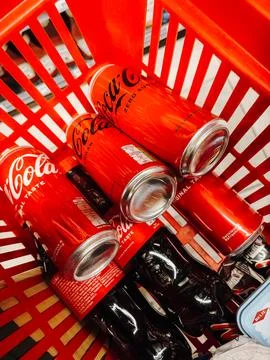Red Coca Cola cans and bottles inside a shopping basket in a grocery store. B Stock Photos