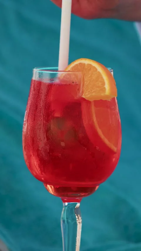 Red cocktail drink being stirred with white straw and orange slice garnish .. Stock Footage 339782881