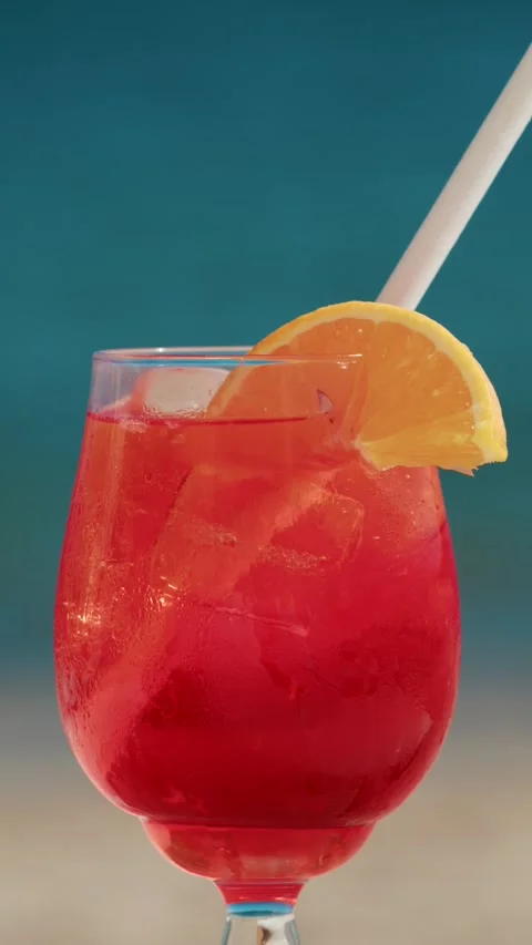 Red cocktail with orange slice and straw against blue tropical sea background Stock Footage 339641908