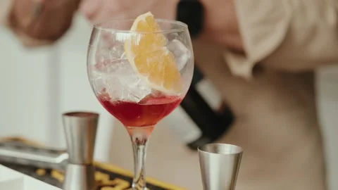 Red Cocktail with Orange Slice and Ice in a Balloon Glass at a Bar Stock Footage 343697535
