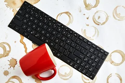 Red coffee cup overturned on a computer keyboard on a table with coffee stains Stock Photos