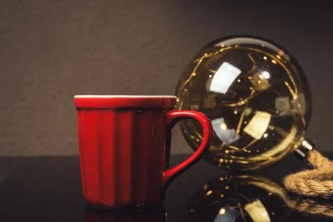 A red coffee cup sits on a table next to a glass sphere Stock Photos