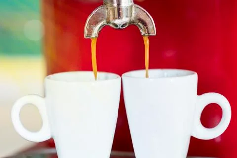 Red coffee machine pours two espresso under the rays of the morning sun Stock Photos