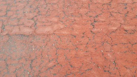 Red colored damaged road or paved pathway with crackes of different shpaes. C Stock Photos