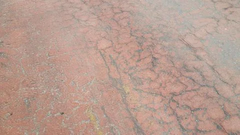 Red colored damaged road or paved pathway with crackes of different shpaes. C Stock Photos