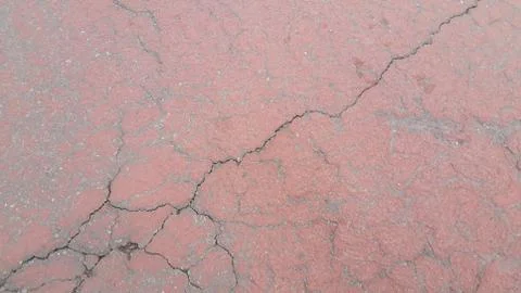 Red colored damaged road or paved pathway with crackes of different shpaes. C Stock Photos