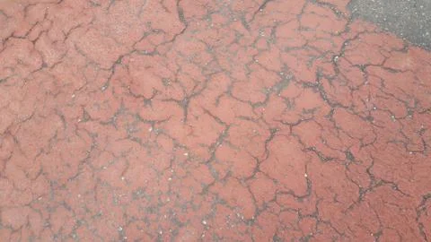 Red colored damaged road or paved pathway with crackes of different shpaes. C Stock Photos