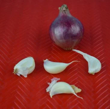A red colored medium sized fresh onion and some scattered garlic seed Stock Photos
