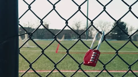 Red Combination Lock Hanging on Chain Link Fence Near Sports Field Stock Footage 328493410