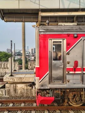 Red commuter train stopping at an elevated urban station platform. Stock Photos