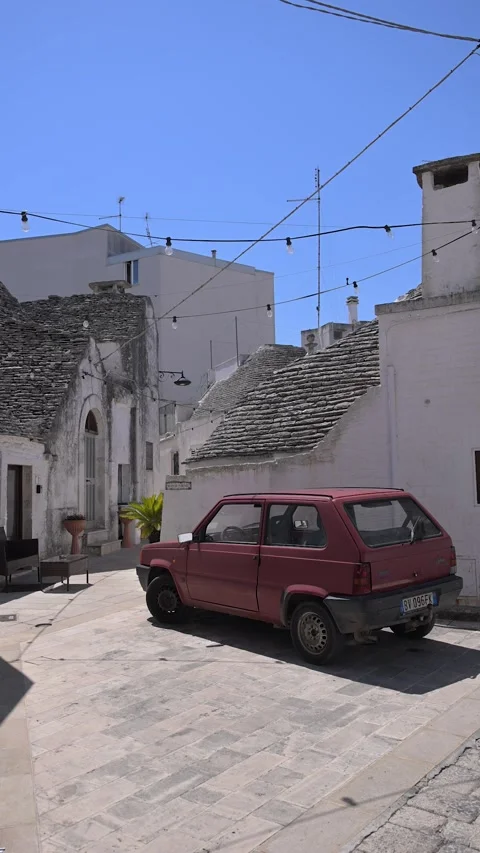 Red Compact Car Parked Beside Traditional Trulli Houses in Alberobello Stock Footage 345319729