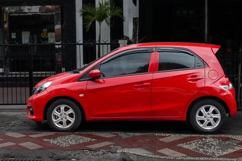 Red Compact Hatchback Car Parked on Urban Street Side with Decorative Pavem.. Stock Photos