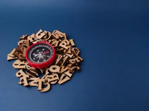 A red compass keychain is surrounded by a pile of scattered wooden letter t.. Stock Photos