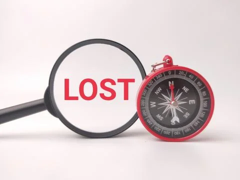 A red compass stands on a white surface next to a magnifying glass framing .. Stock Photos