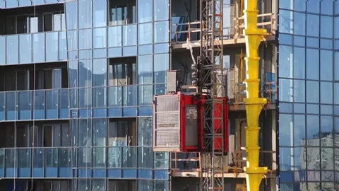 A red construction elevator rising along the facade of a modern glass building Stock Footage 320997017