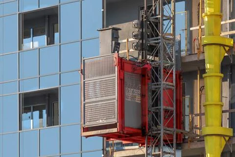 A red construction elevator rising along the facade of a modern building Stock Photos