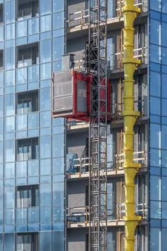 A red construction elevator rising along the facade of a modern building Stock Photos