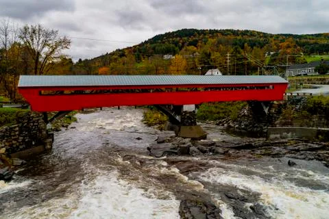 A red covered bridge first built in 1883 spans a rapidly flowing river Stock Photos