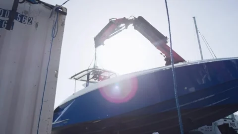 Red Crane Hoisting Blue Motor Yacht Hull, Boatyard Sun Flare, Low Angle Shot Stock Footage 340333142