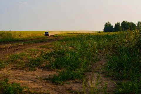 Red crossover raises a cloud of dust on a country dirt road. The road along t Stock Photos