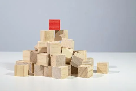 Red cube standing on the top of a heap from light wooden cubes, concept for Stock Photos