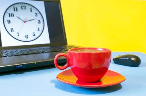 Red Cup of coffee on a blue table on the background of the laptop screen cloc Stock Photos