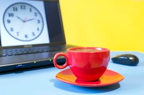 Red Cup of coffee on a blue table on the background of the laptop screen cloc Stock Photos
