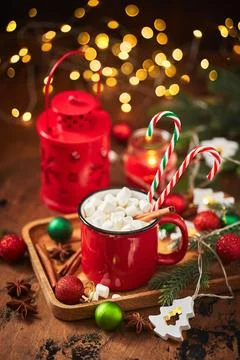 Red cup of hot cocoa with marshmallows and candy canes on wooden table with c Stock Photos
