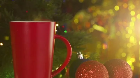 Red cup of steaming coffee next to a decorated Christmas tree Stock Footage 56733590