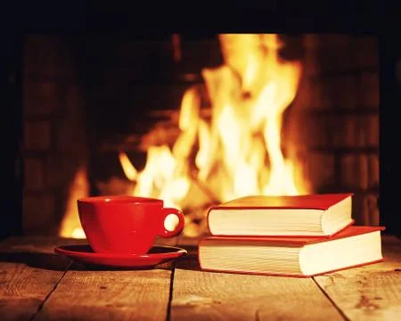 Red cup of tea or coffee and old books near fireplace.. Stock Photos