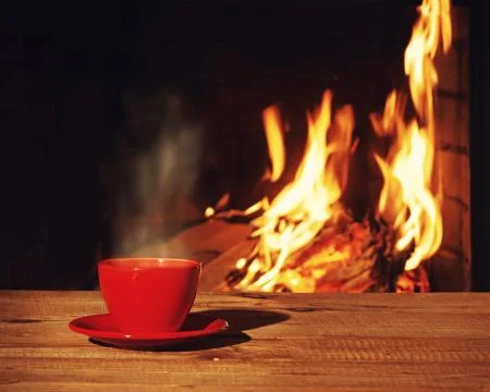 Red cup of tea or coffee near fireplace on wooden table. Stock Photos