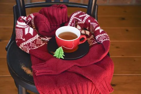 A red cup with tea is wrapped in a warm Christmas sweater, a tea bag label Stock Photos