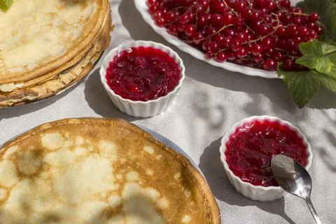 Red currant jam on the table with freshly baked thin pancakes. Traditional Ru Stock Photos