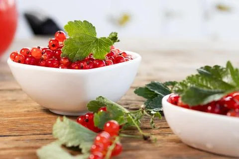 Red currants piled in white ceramic bowl with glossy green leaf, scattered Stock Photos
