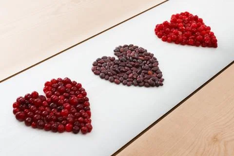 Red current, cranberries and beans in heart shape on wooden board Stock Photos