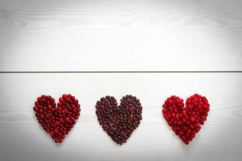 Red current, cranberries and beans in heart shape on wooden board Stock Photos