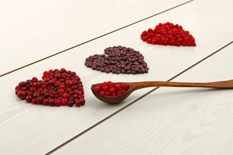 Red current, cranberries and beans in heart shape on wooden board Stock Photos